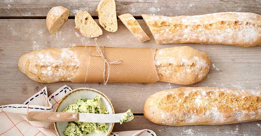 Baguettes auf dem Holztisch mit Kräuterbutter im Schälchen