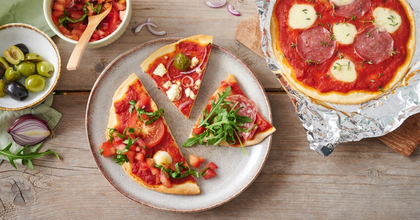 Bunt belegte Pizza auf dem Teller und auf Toppits Recycling Alufolie