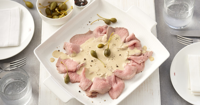 Vitello Tonnato auf einem Teller dekoriert mit Kapernäpfeln